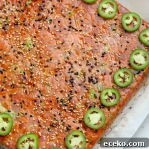 Spicy Tuna Oshizushi: Pressed Sushi Recipe 10 Overhead view of spicy tuna pressed sushi on parchment, topped with black and white sesame seeds and a border of sliced jalapeños.