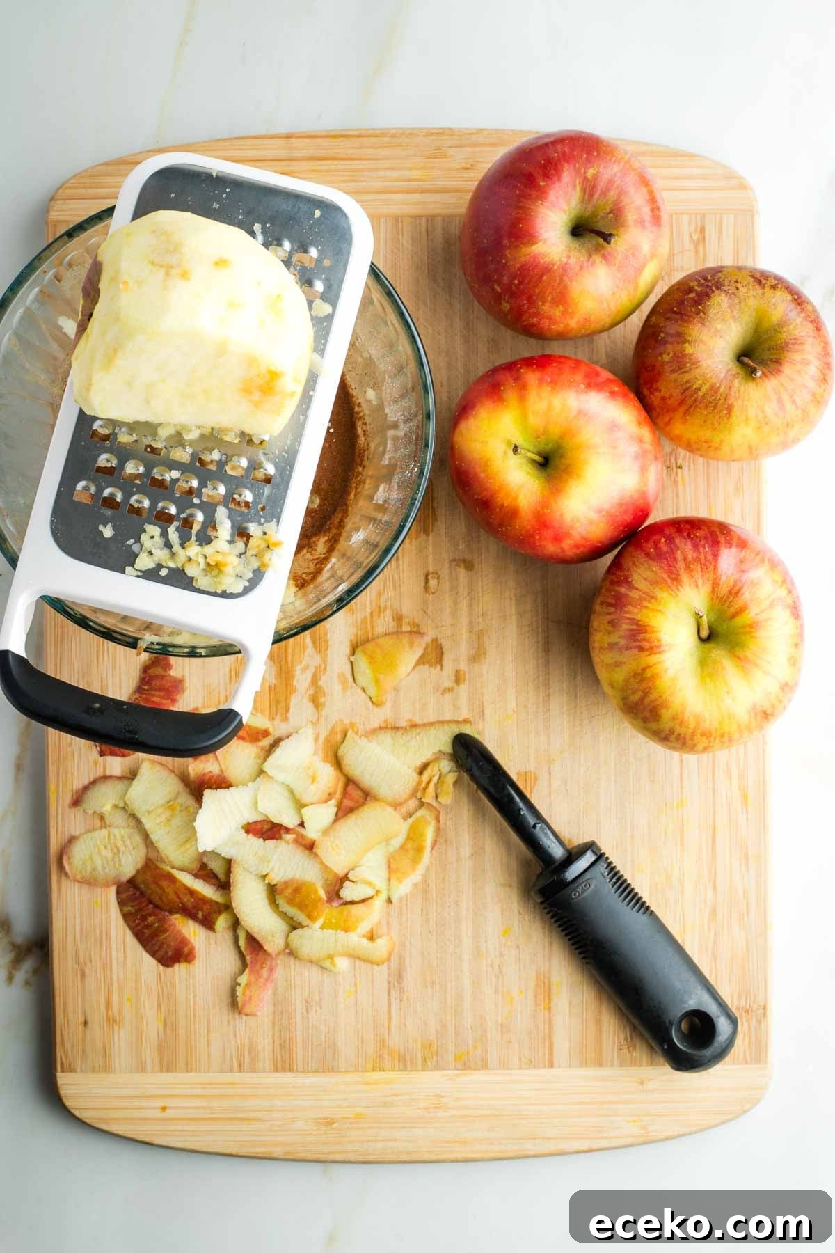 Vegan Apple Pie Bars with Cinnamon Streusel 16 Apples, and apple peels, plus a peeled apple being grated into a glass bowl.