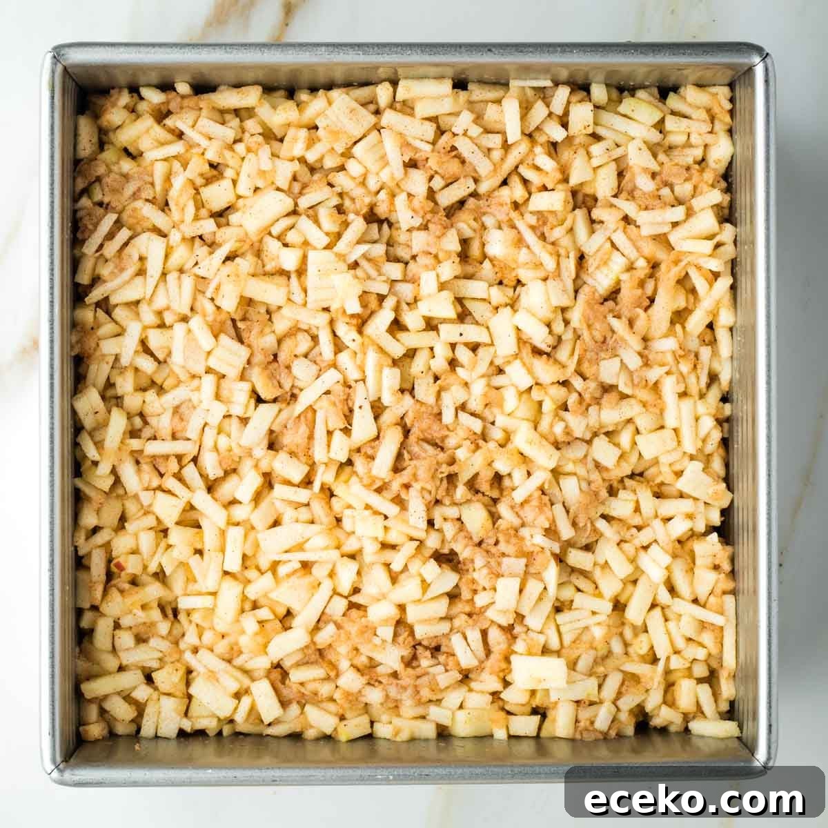 Vegan Apple Pie Bars with Cinnamon Streusel 18 Small pieces of apples and spices in a square pan on top of a piece of pie dough.