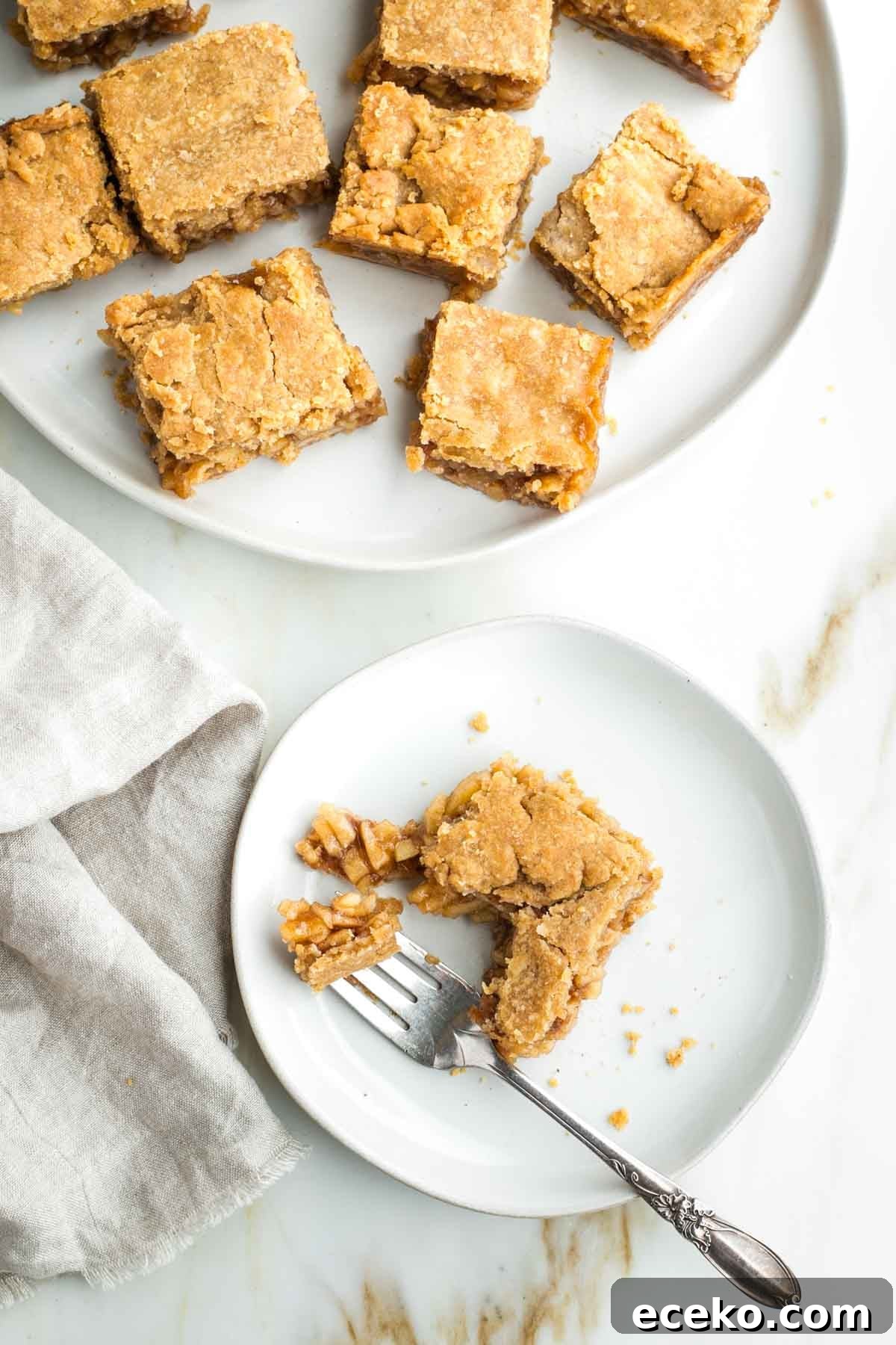 Vegan Apple Pie Bars with Cinnamon Streusel 24 Apple pie bars, and one on a plate being eaten with a fork, showing the inside pieces of apples.