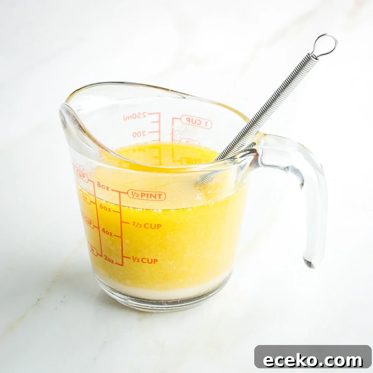 Vegan Apple Pie Bars with Cinnamon Streusel 5 Whisk inside a one cup pyrex measuring cup filled with yellow liquid.