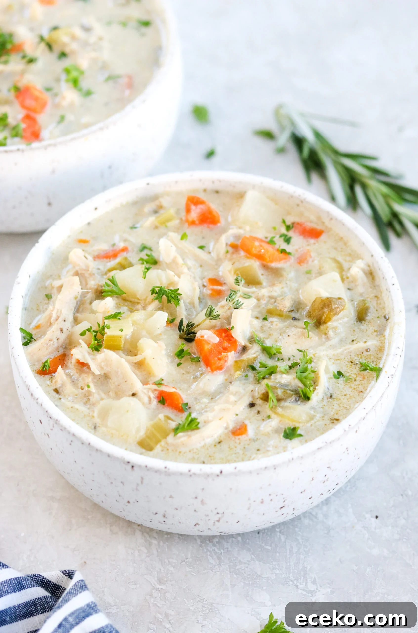 Creamy Chicken Pot Pie Soup with Vegetables 2 Paleo Chicken Pot Pie Soup with chicken, carrots, celery, and herbs in a white bowl on a gray surface with rosemary