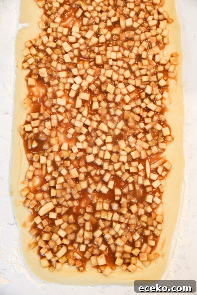 Cinnamon Rolls Stuffed with Apple Pie Filling 6 Dough rolled out flat and topped with a mixture of small diced apples and cinnamon filling, just like Apple Pie Filled Cinnamon Rolls, ready to be rolled or baked.