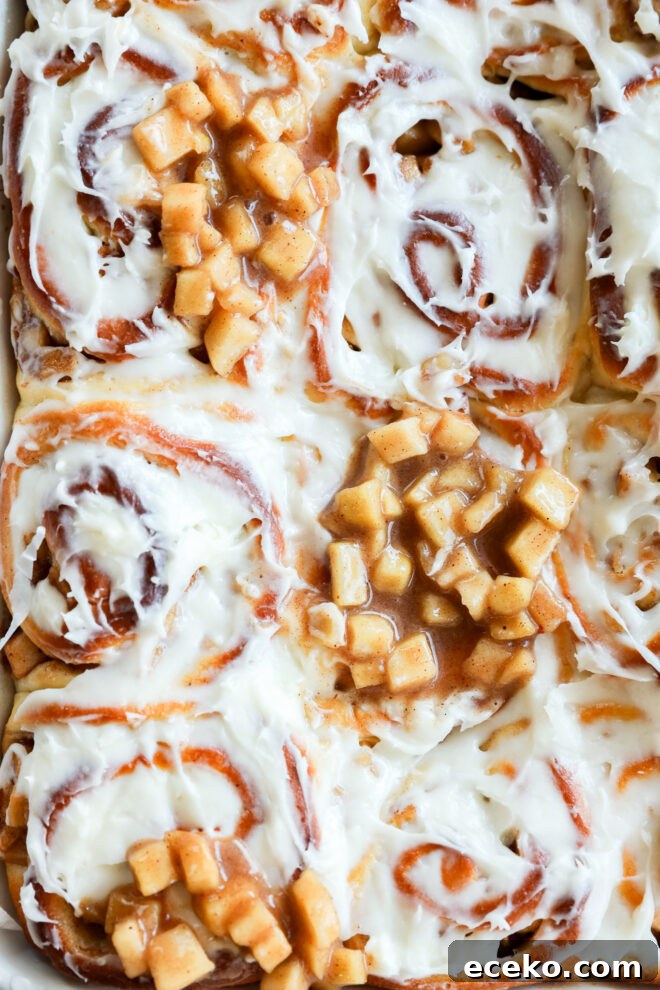 Cinnamon Rolls Stuffed with Apple Pie Filling 8 Close-up of Apple Pie Filled Cinnamon Rolls topped with creamy white frosting and diced cooked apples in cinnamon sauce, creating a gooey and appealing texture.