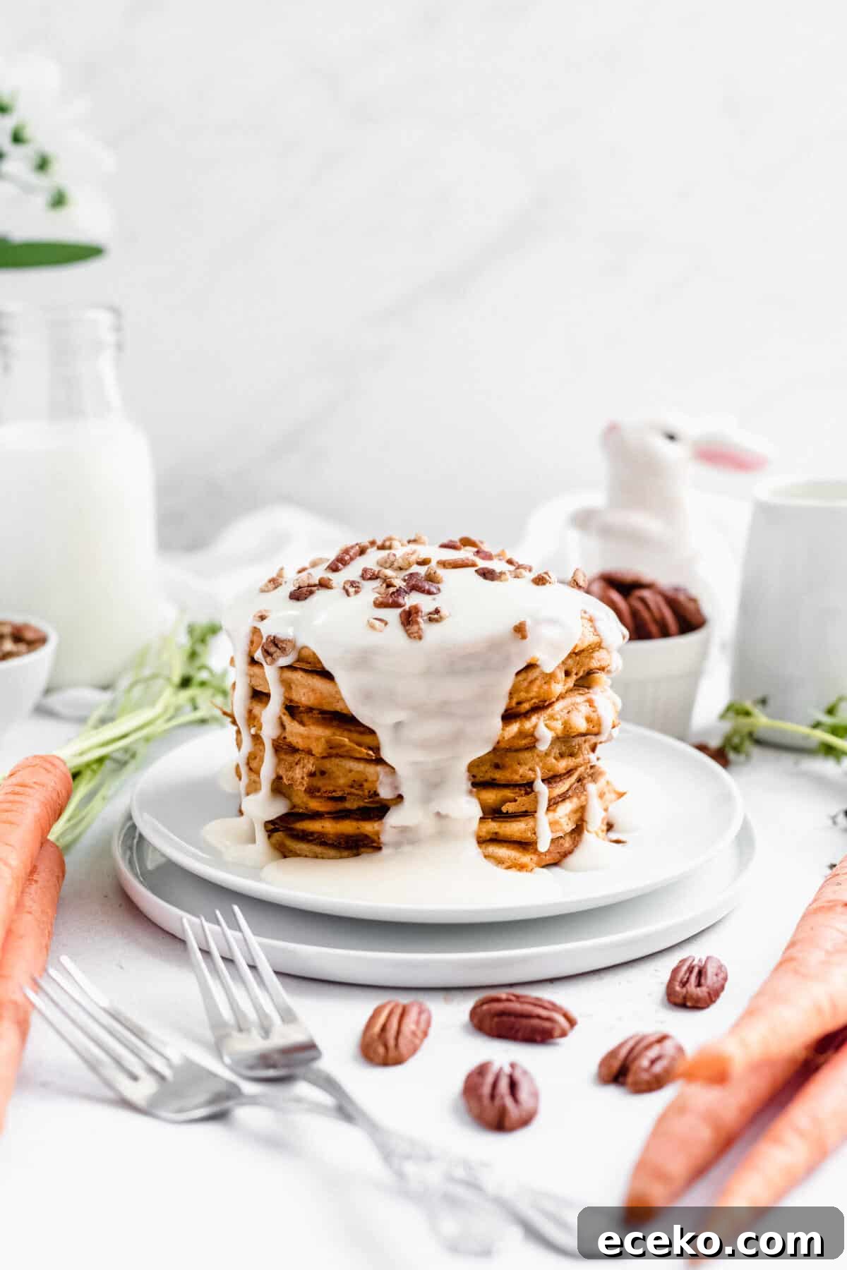 Carrot Cake Pancake Recipe with Cream Cheese Glaze 2 pancake stack on two white plates with two forks, carrots and pecans around it