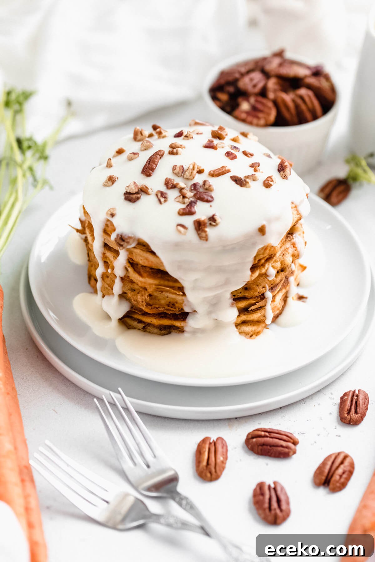 Carrot Cake Pancake Recipe with Cream Cheese Glaze 3 stack of pancakes topped with cream cheese glaze and chopped pecans