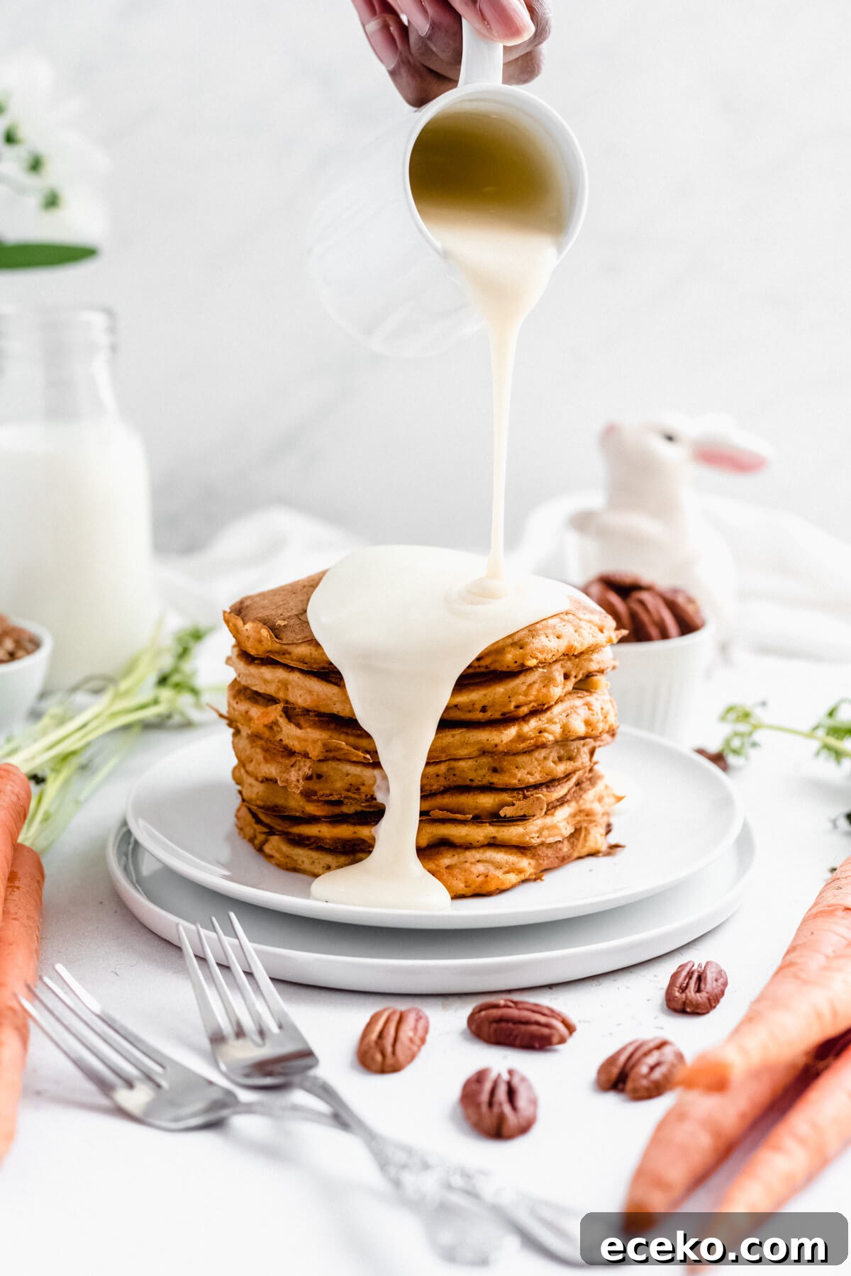 Carrot Cake Pancake Recipe with Cream Cheese Glaze 5 pouring cream cheese glaze onto a stack of pancakes